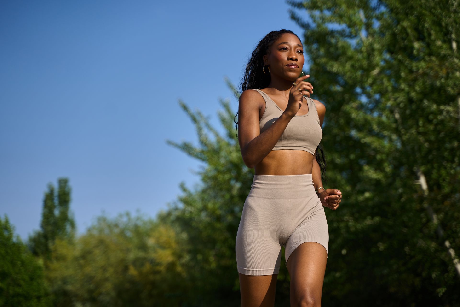 Woman jogging outdoors in beige athletic wear under a clear blue sky.