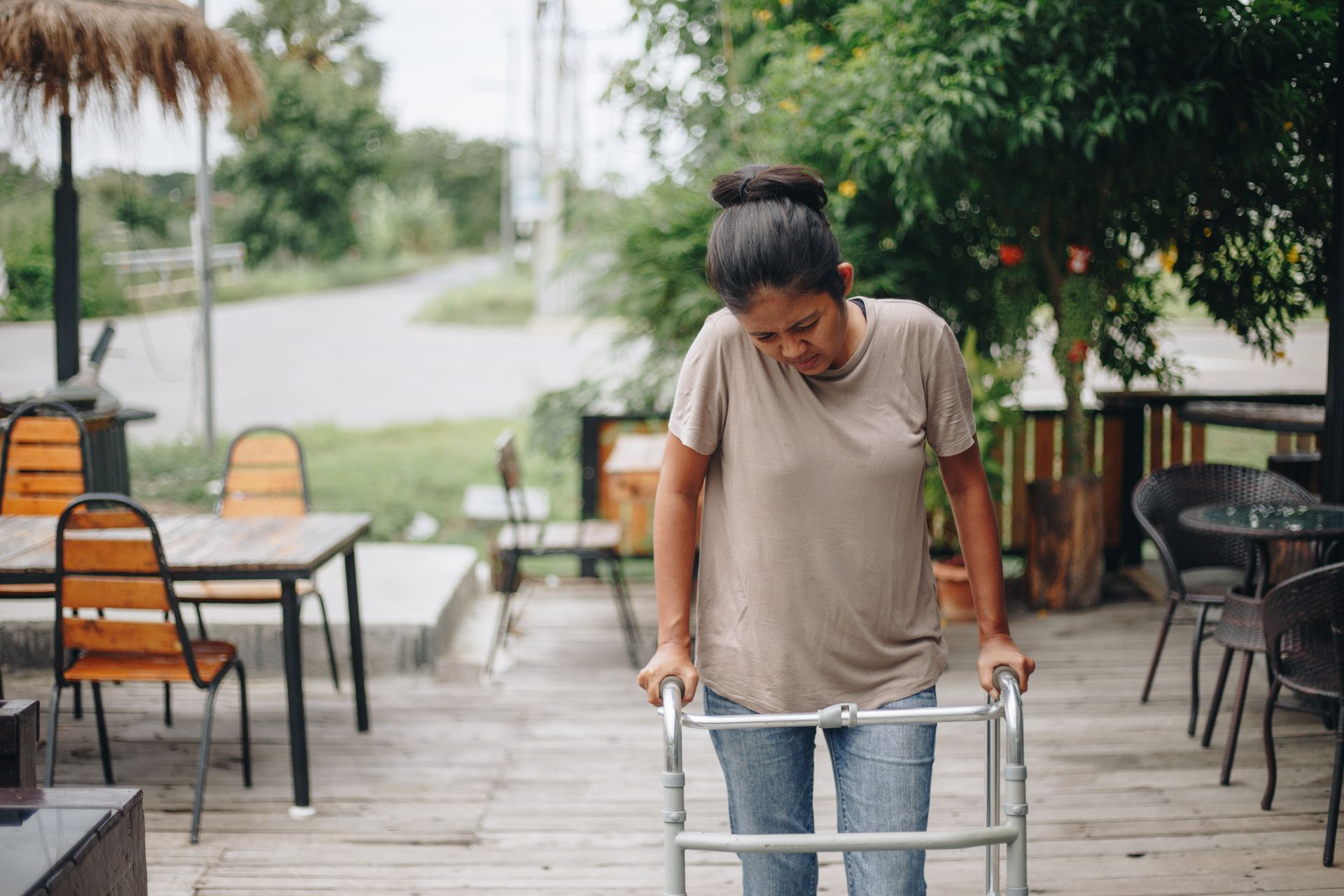 Woman pushing a walker on a wooden patio beside outdoor café tables and chairs