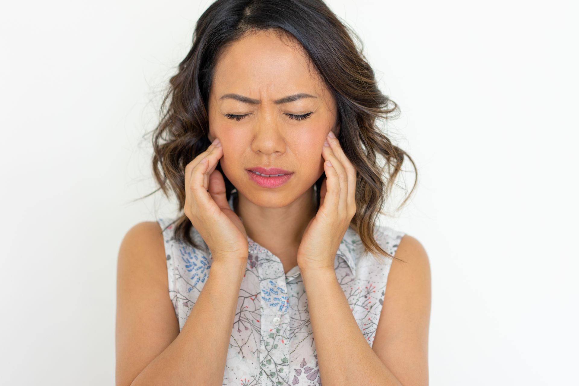 Woman holding her temples with eyes closed, looking in pain against a white background