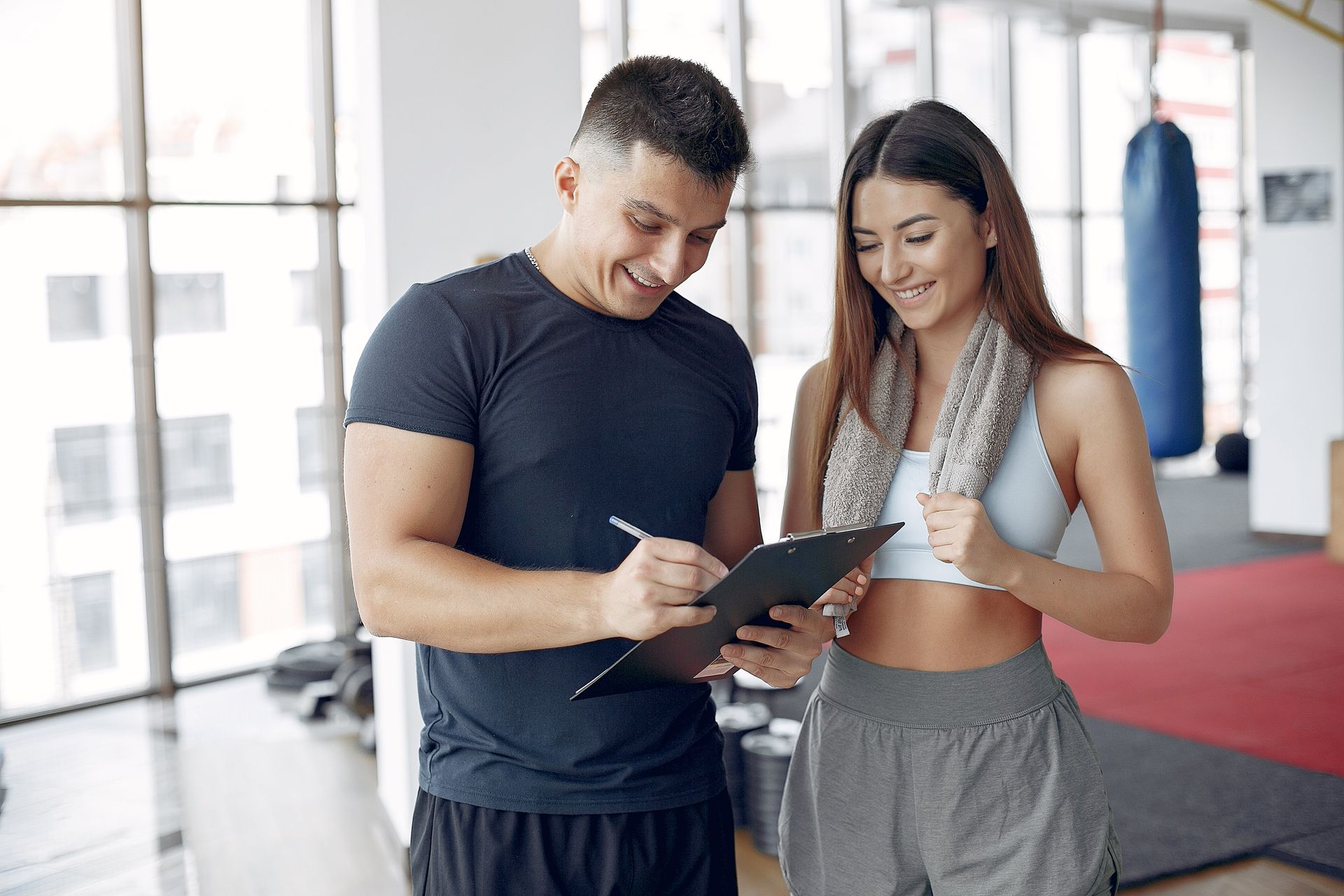 Two people reviewing a tablet together in a bright gym, with exercise equipment in the background.