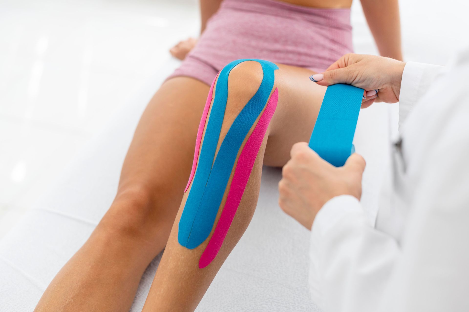 Physiotherapist applying blue and pink kinesiology tape to a patient’s thigh and knee