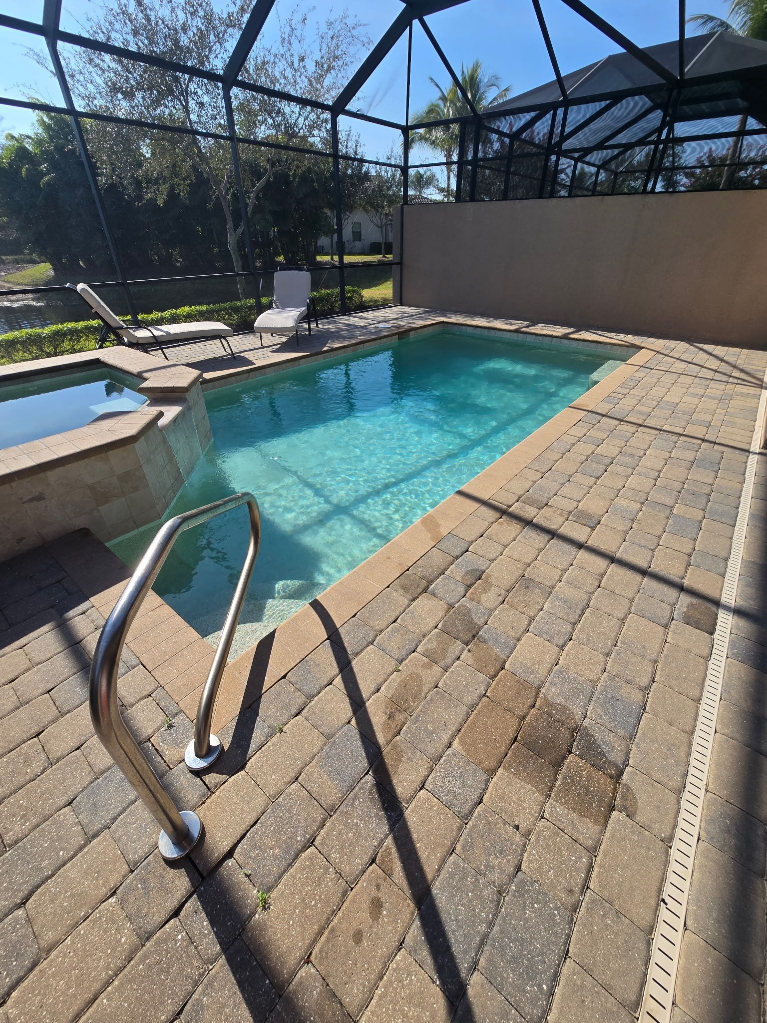 Small outdoor pool with brick patio, surrounded by a screen enclosure and a spa.