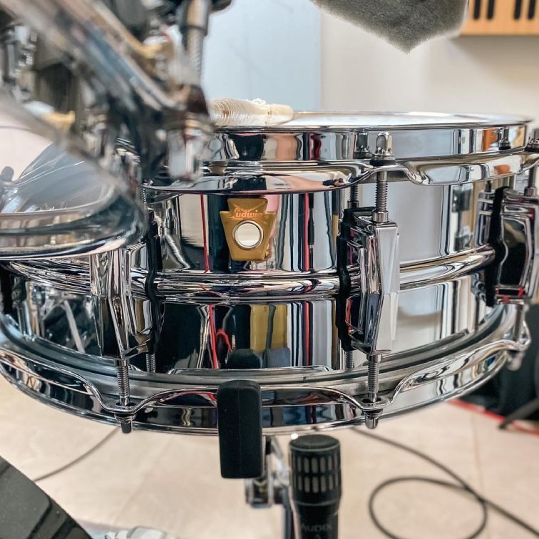 Shiny chrome snare drum, with gold badge, mounted on stand, in studio.