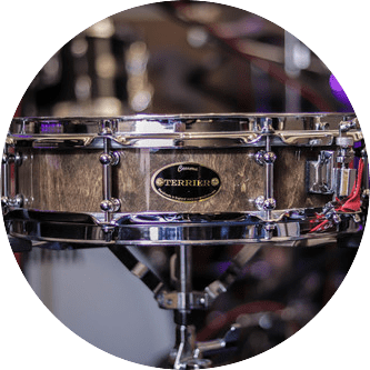 A close-up of a snare drum with a dark wooden body and silver hardware, in a drum set.