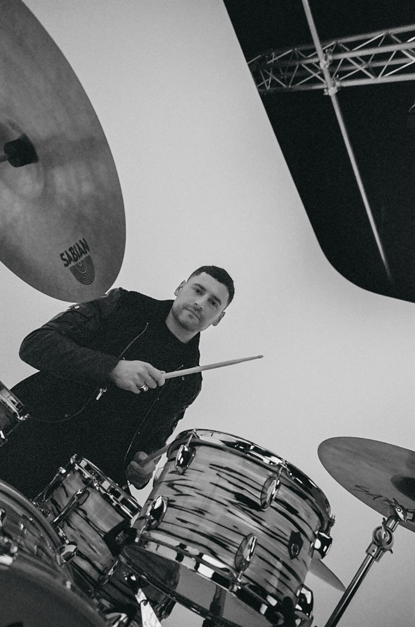 Smiling man playing drums in a studio, holding a drumstick.