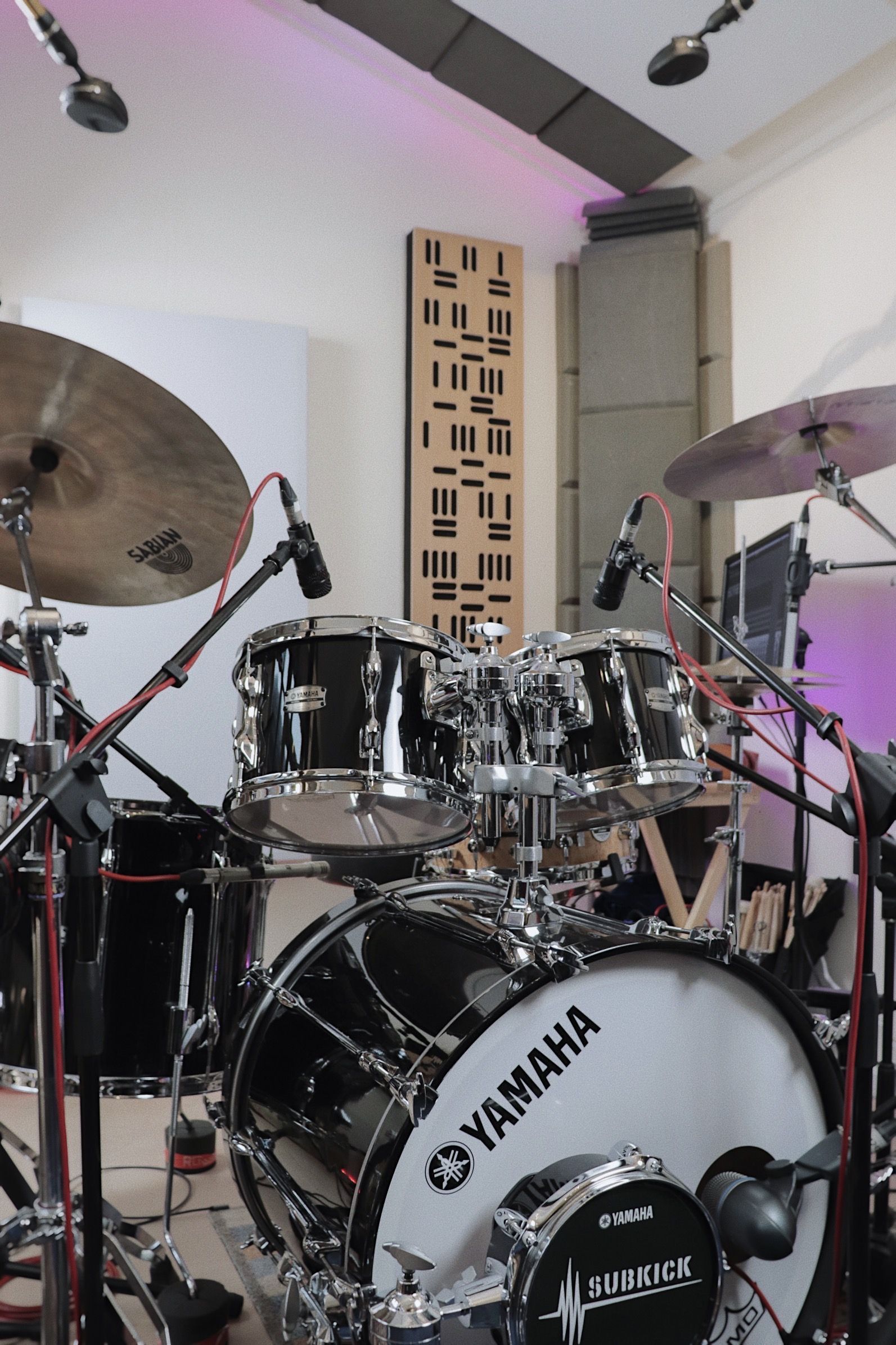 Drum set in a studio with microphones, sound panels, and Yamaha logo. Black and chrome drums.