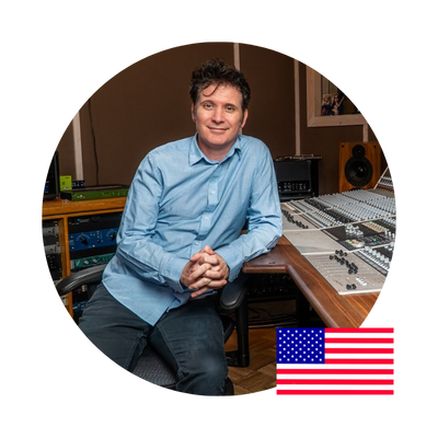 Man in recording studio, hands clasped, wearing a blue shirt. US flag.