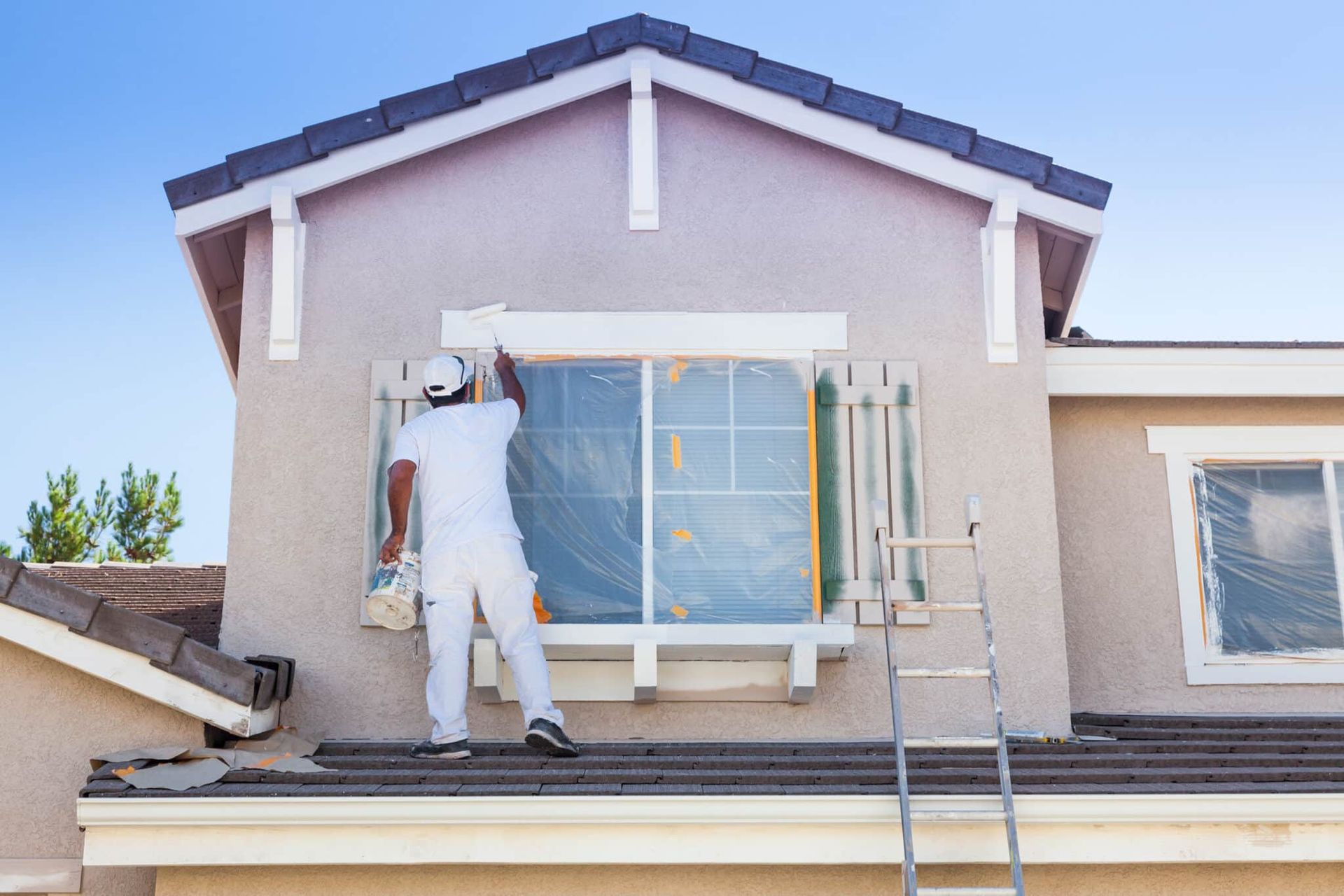 A man is painting a window on the side of a house.