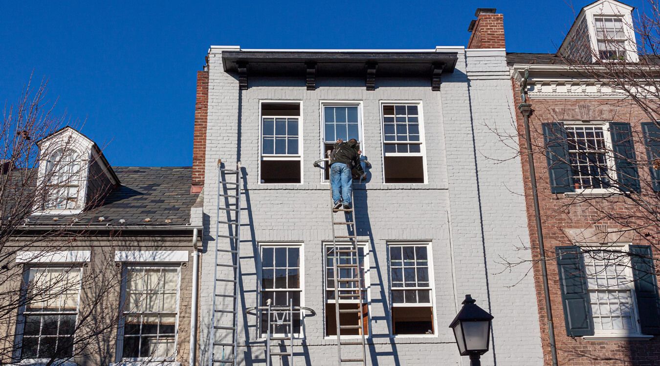 A man is standing on a ladder on the side of a building.