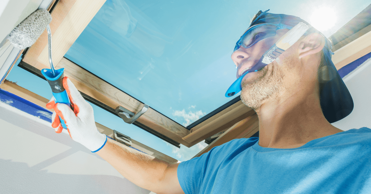 A man is painting a skylight with a brush.