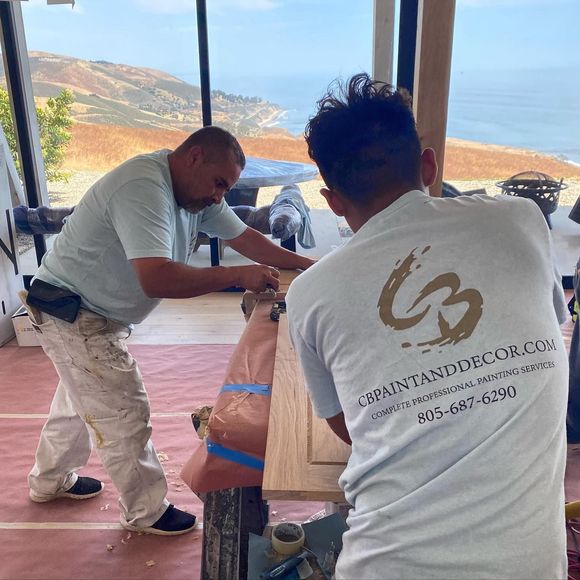 Two men are working on a piece of wood in a room with a view of the ocean.