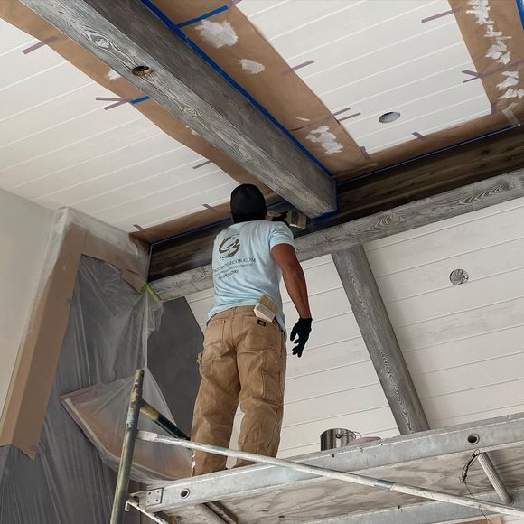 A man is standing on a ladder looking up at the ceiling.