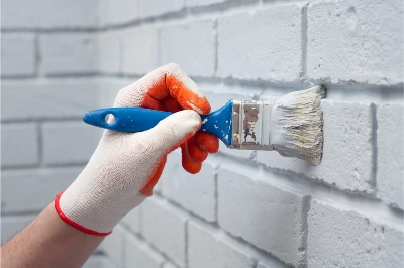 A person is painting a brick wall with a brush.