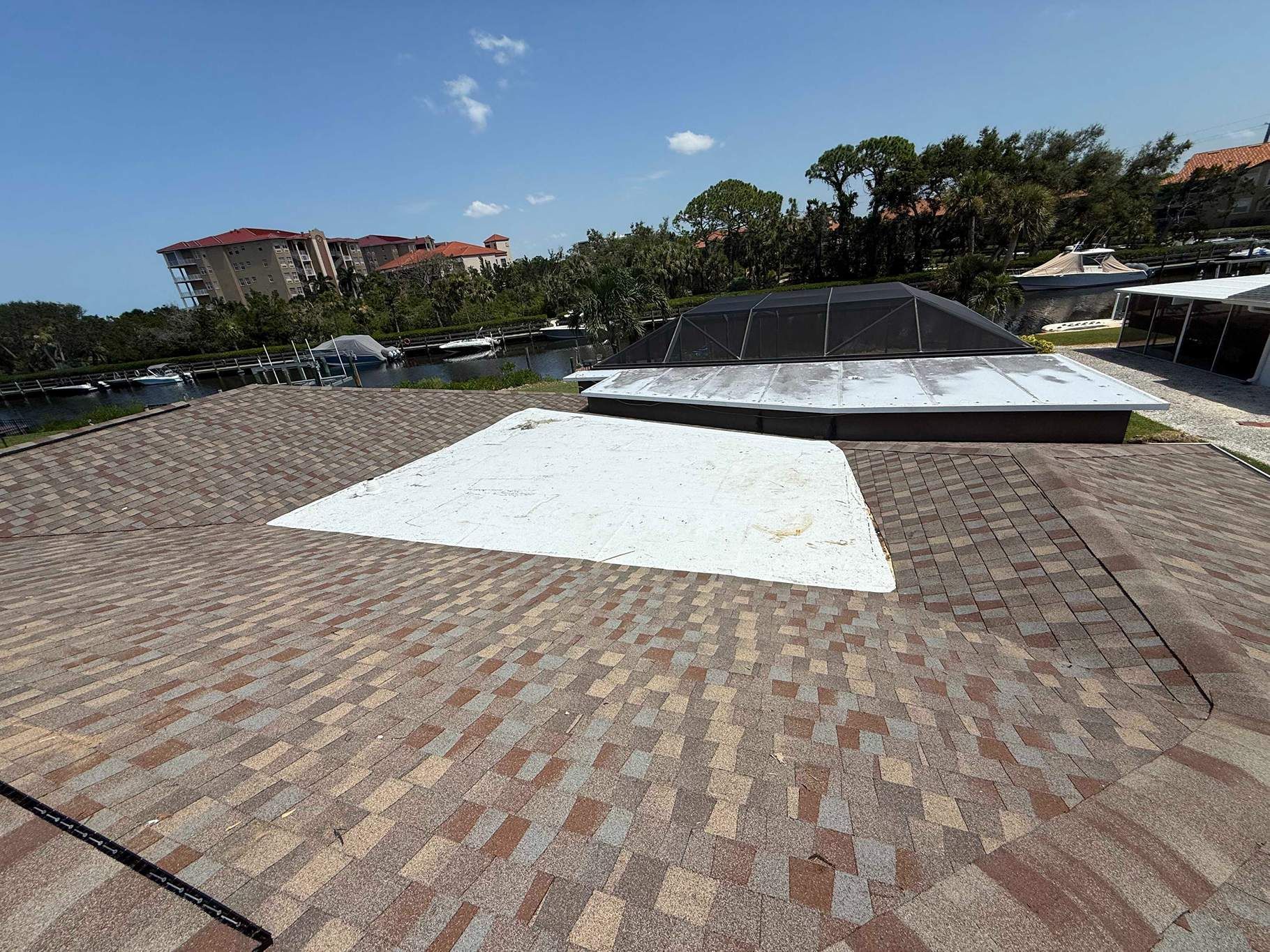 View from a roof with brown shingles, overlooking a body of water and buildings on a sunny day.
