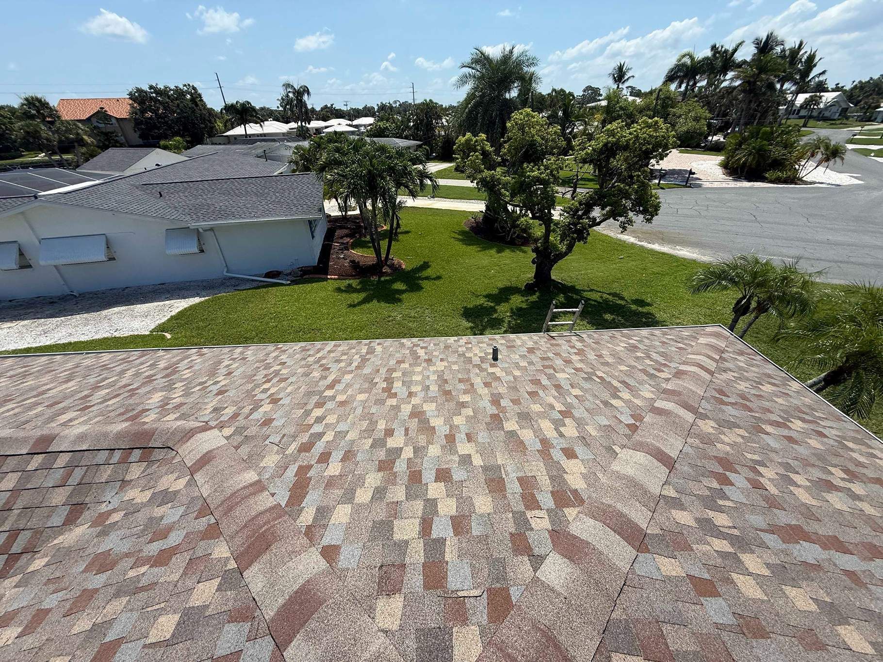 View from a roof, showing shingle texture, green grass, trees, and buildings on a sunny day.