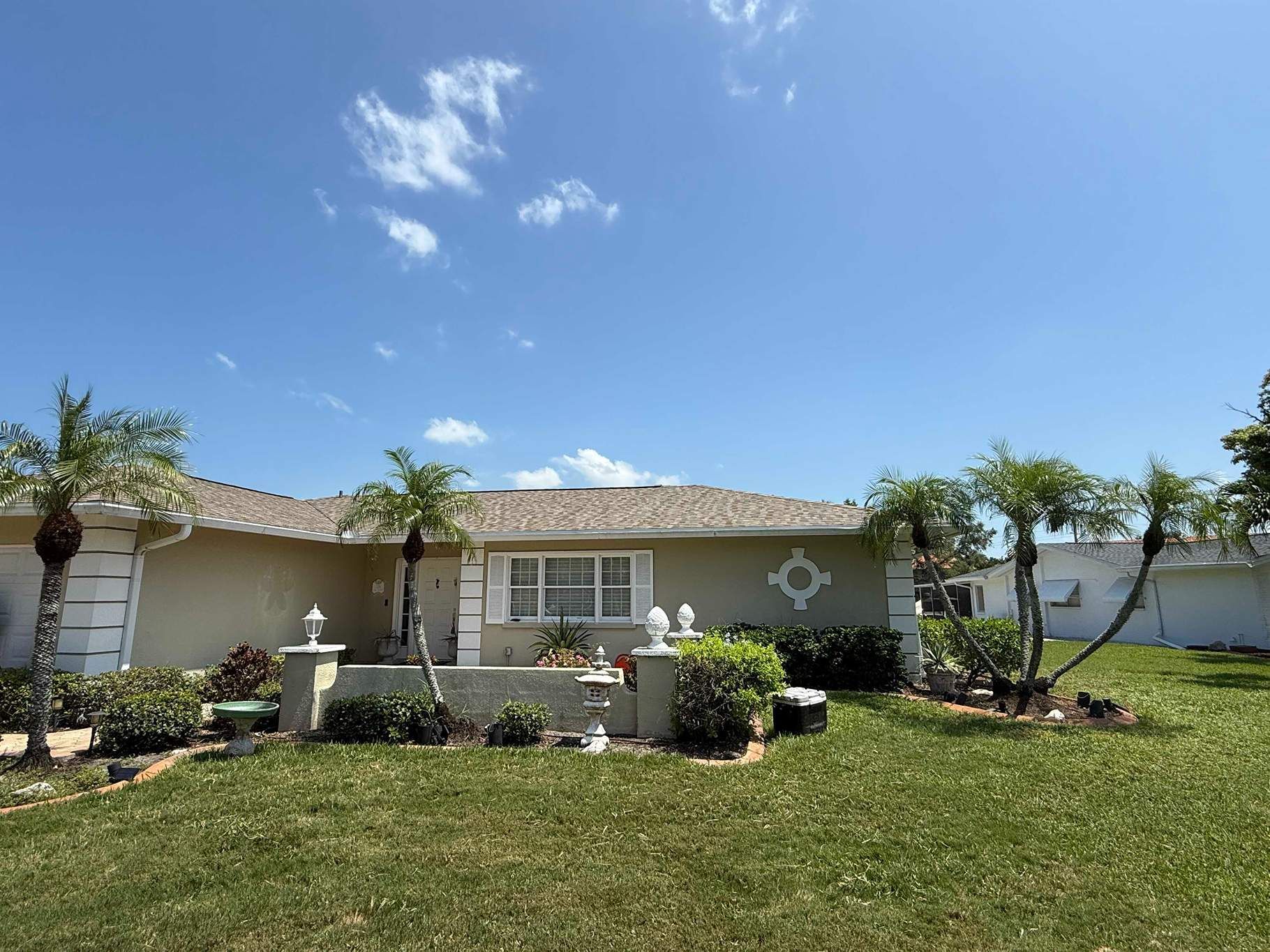 Beige house with palm trees, green grass, and blue sky.