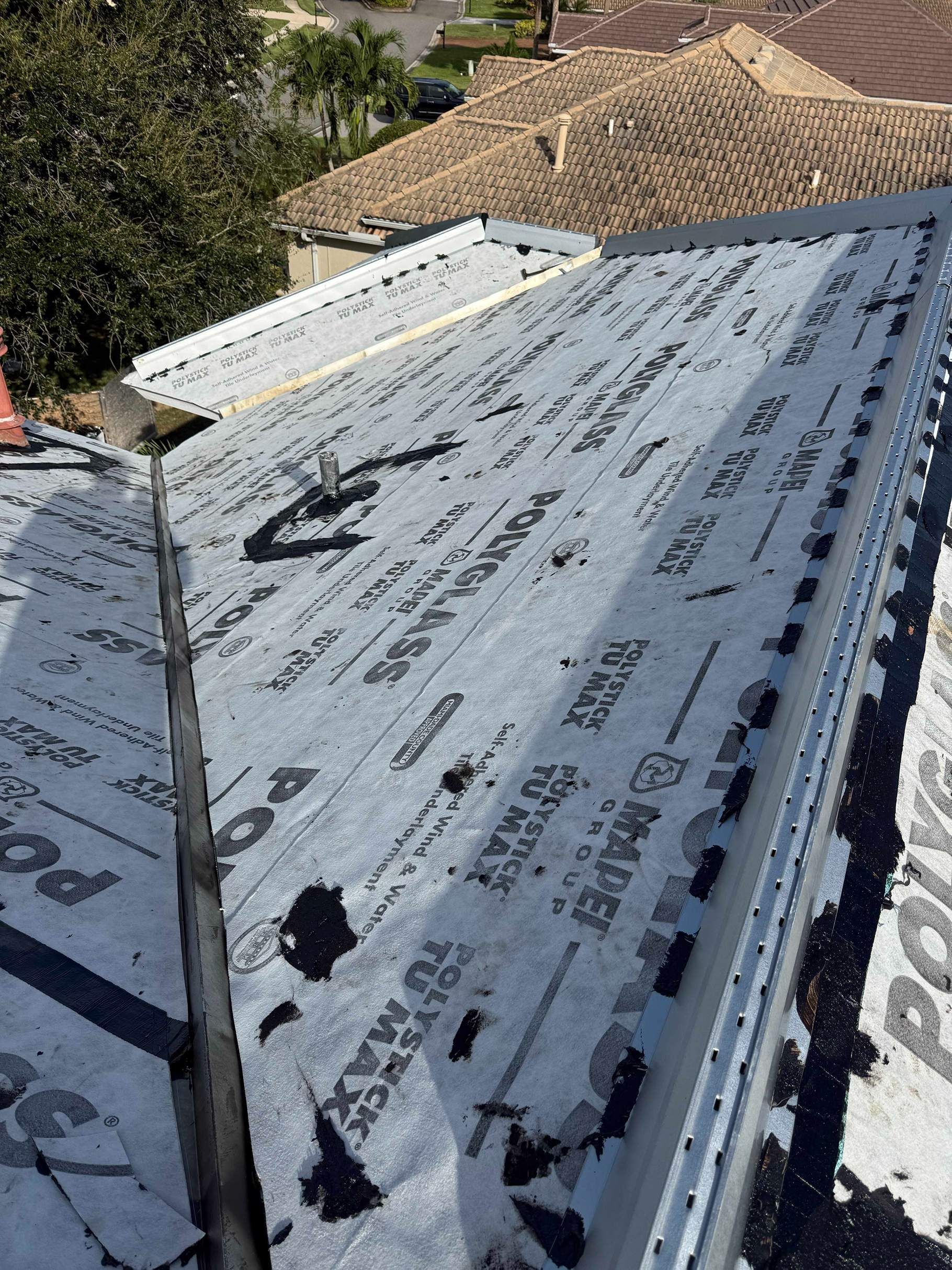 A roof covered in black underlayment with a gutter and a section of roof tiles in the background.