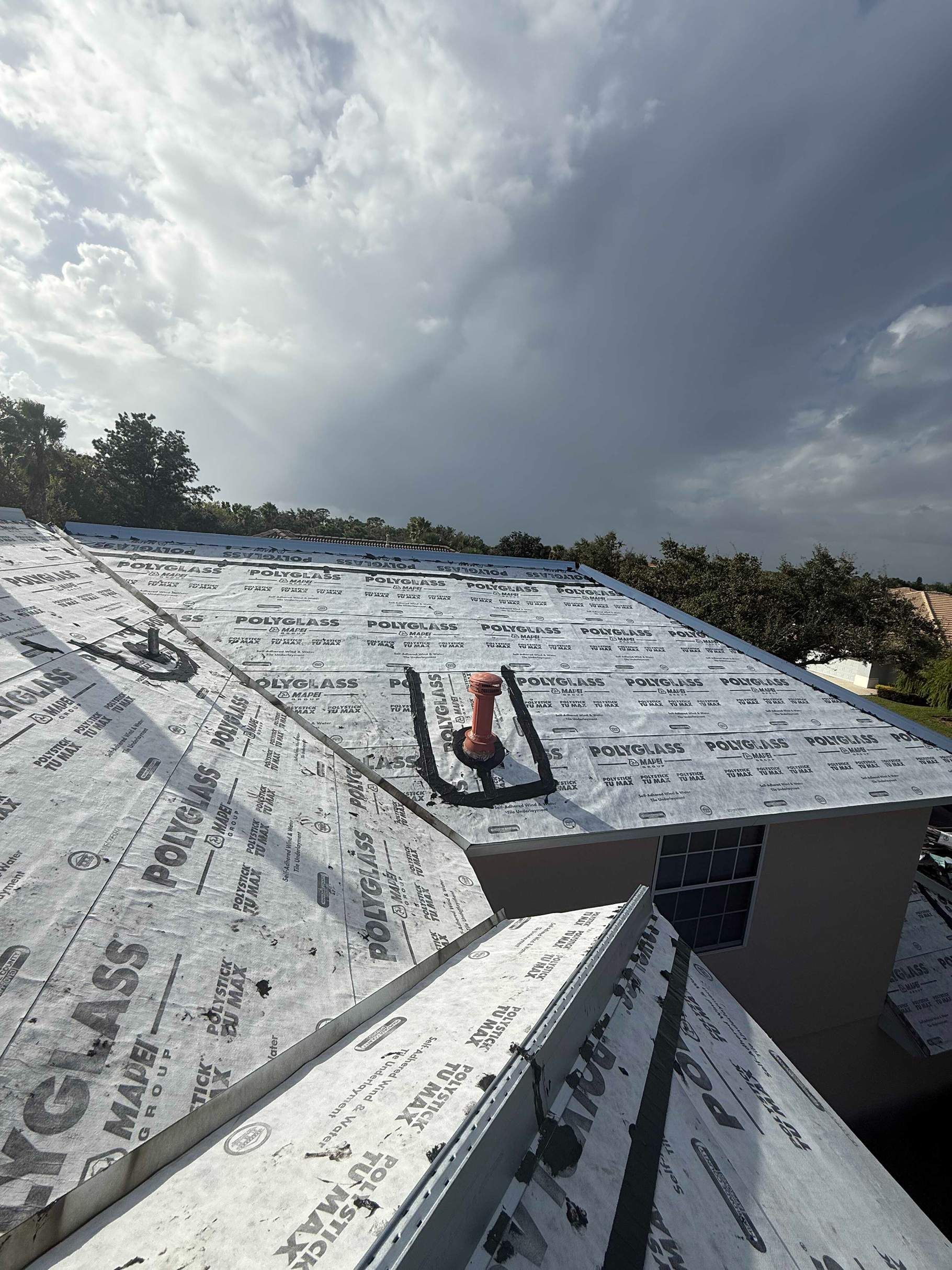 Rooftop with black underlayment, vent pipe, and cloudy sky.