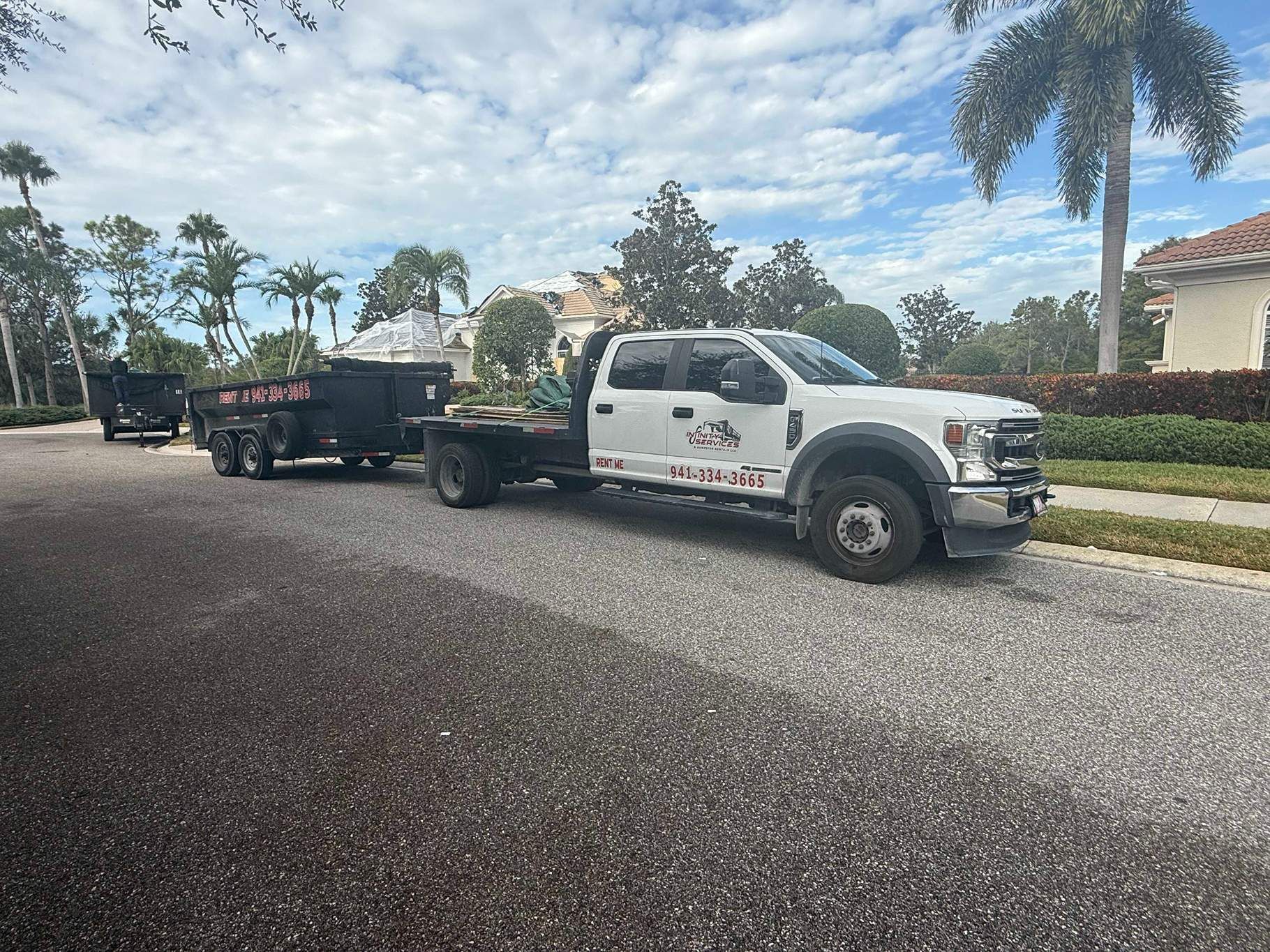 White work truck with trailer on residential street, blue sky.