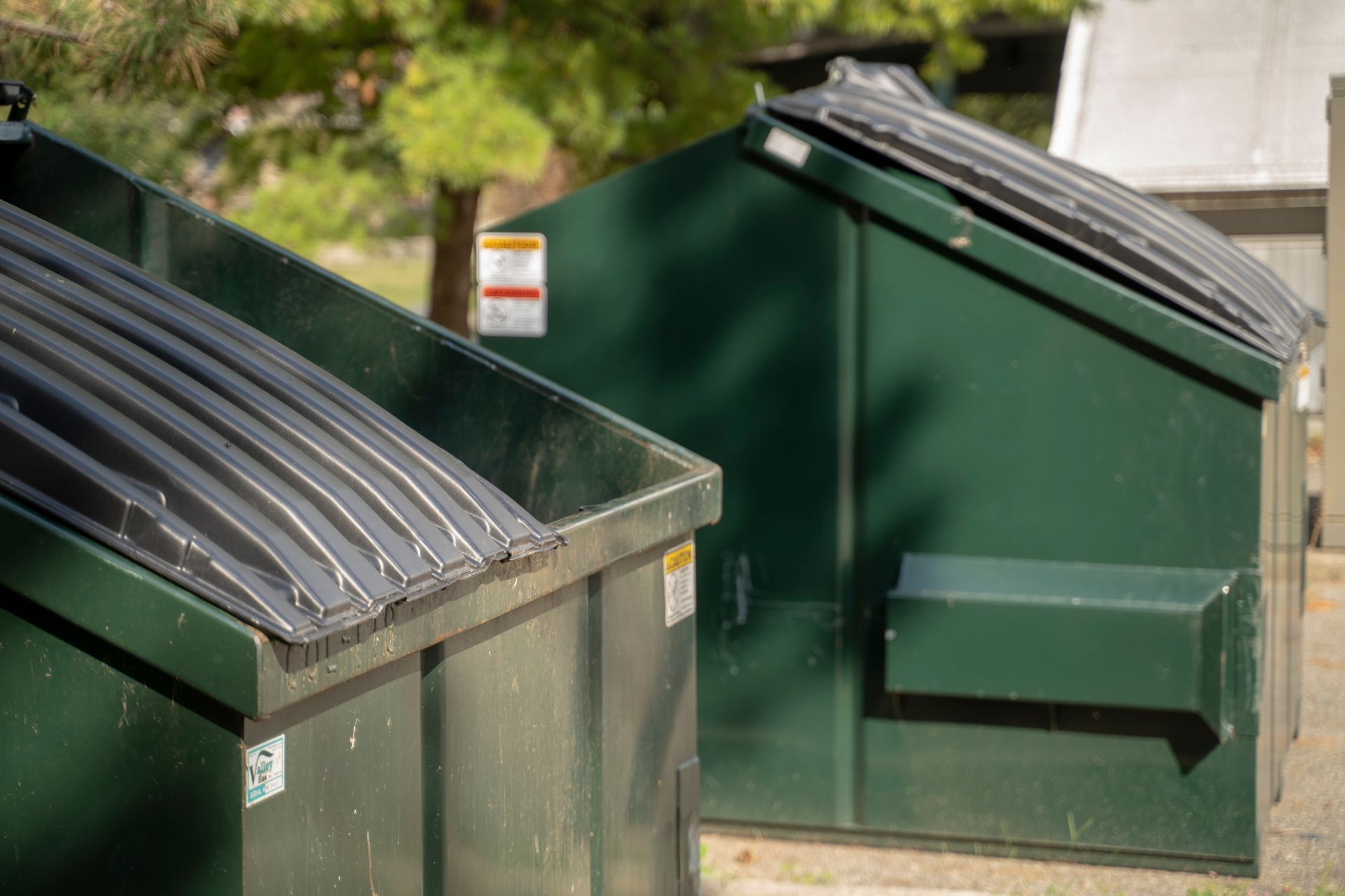 Two dark green dumpsters with black lids, outdoors.