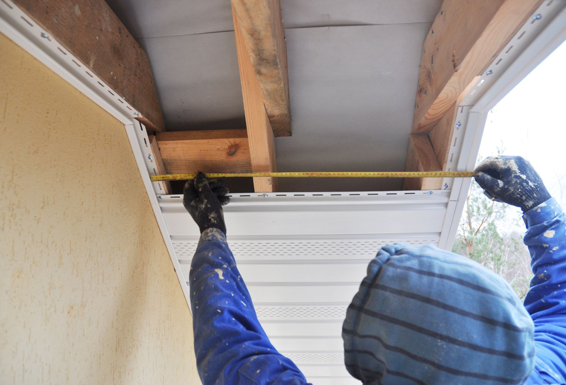 Person measures the width of a soffit with a yellow tape measure, part of house construction.