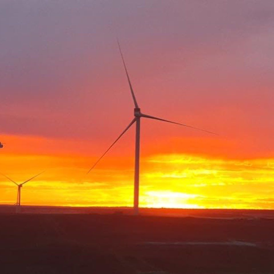 Two wind turbines are silhouetted against a sunset sky.