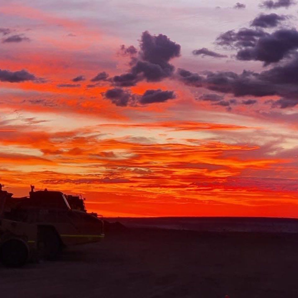 A sunset over a desert with a tractor in the foreground.