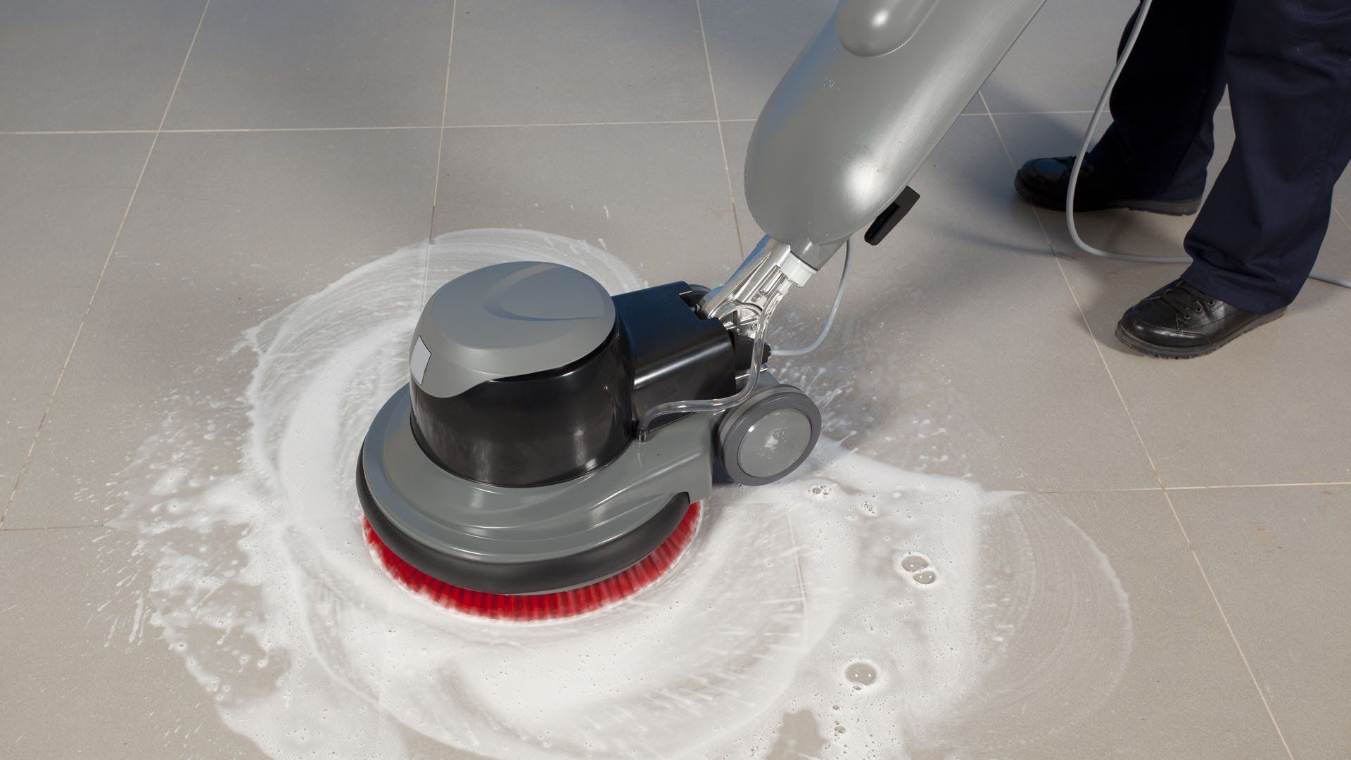 Macchina lavapavimenti che strofina il pavimento piastrellato con un prodotto detergente bianco.