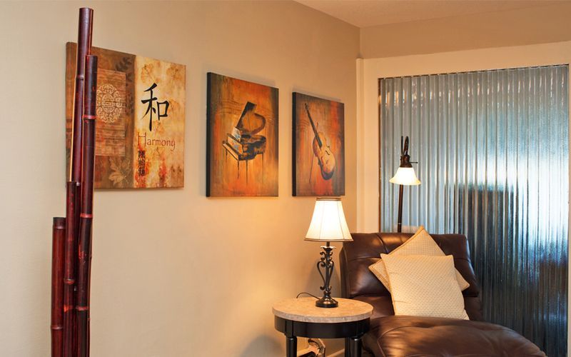 A living room with a couch , table , lamp and paintings on the wall.