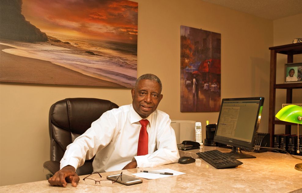 A man in a white shirt and red tie is sitting at a desk with a computer.