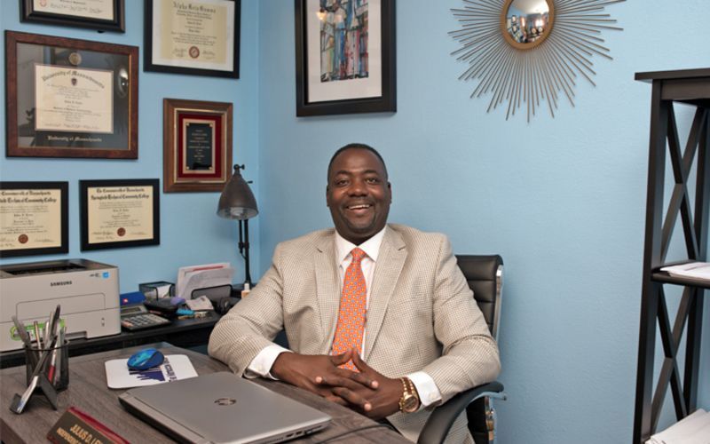 A man in a suit and tie is sitting at a desk with a laptop.