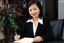 A woman in a suit is sitting at a desk writing on a piece of paper.