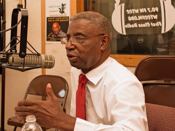 A man in a white shirt and red tie is sitting at a desk with a computer.