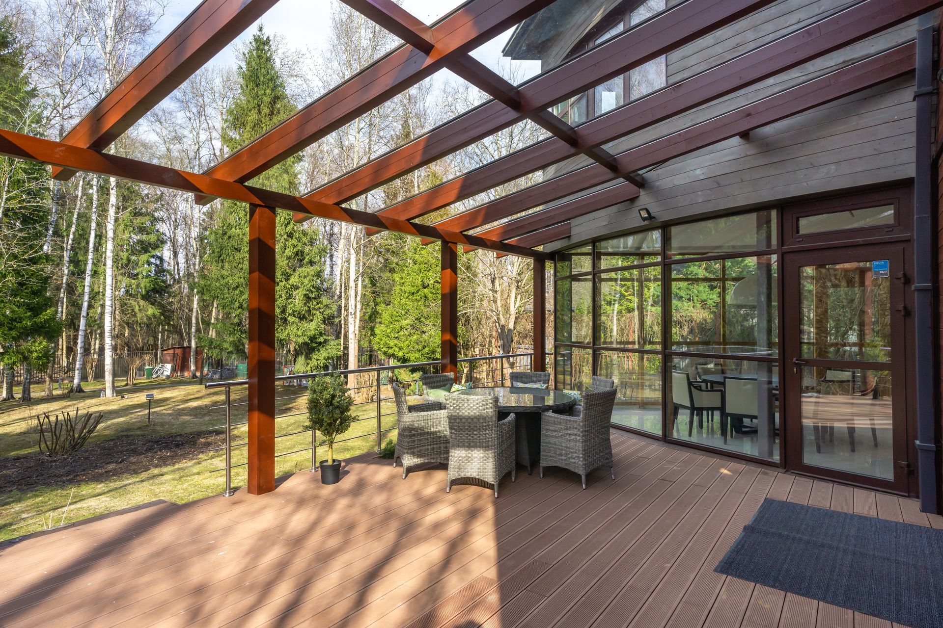 Covered outdoor patio with glass walls, dining table, and chairs beside a wooded yard