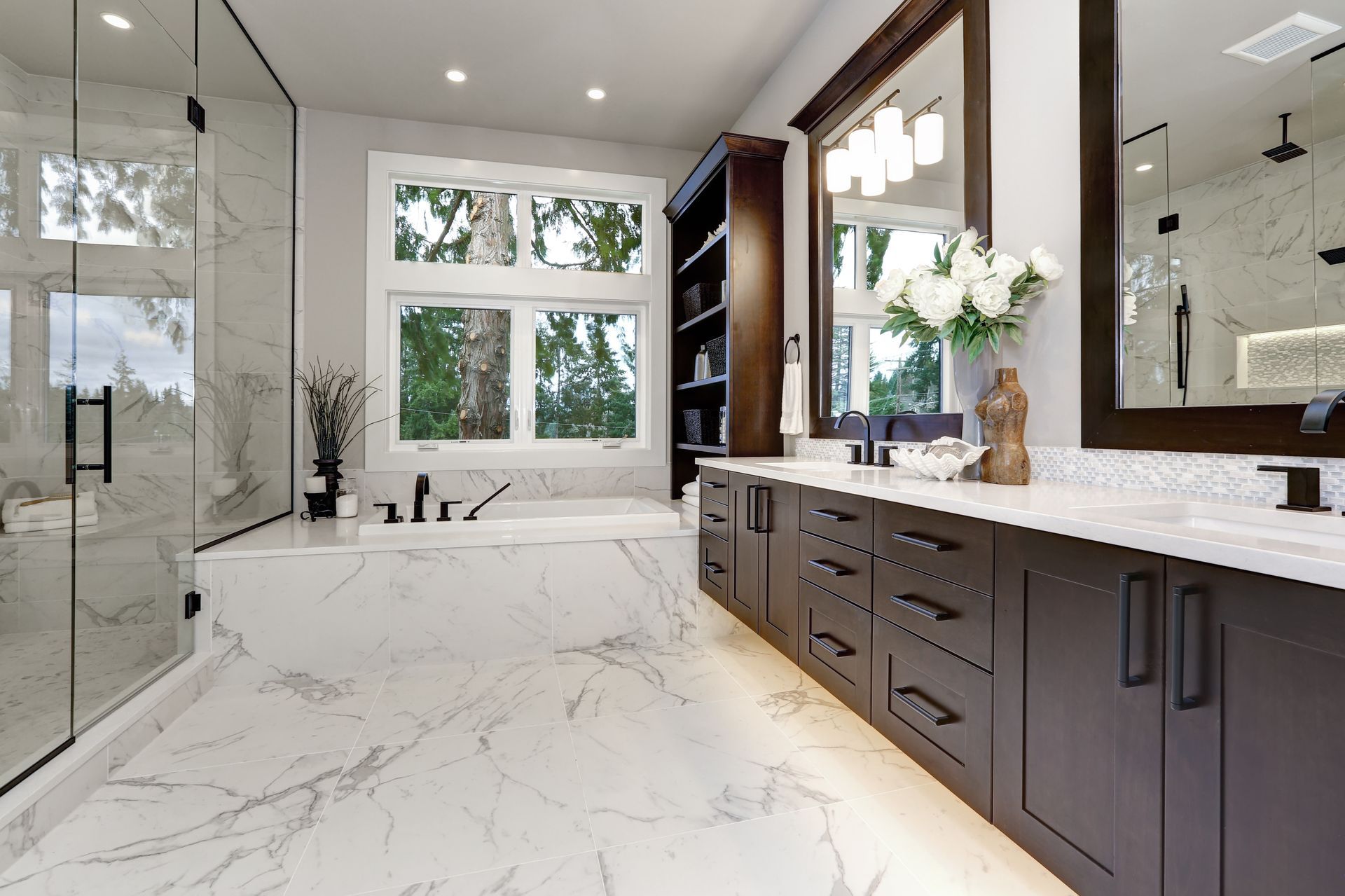 Modern bathroom with marble floors, dark wood vanity, large mirror, and freestanding tub by a window