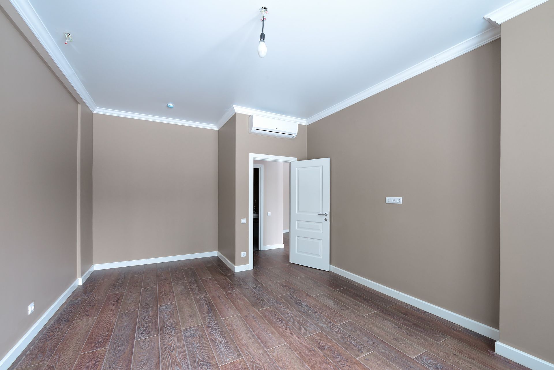 Empty beige room with white trim, dark wood floor, and an open white door.