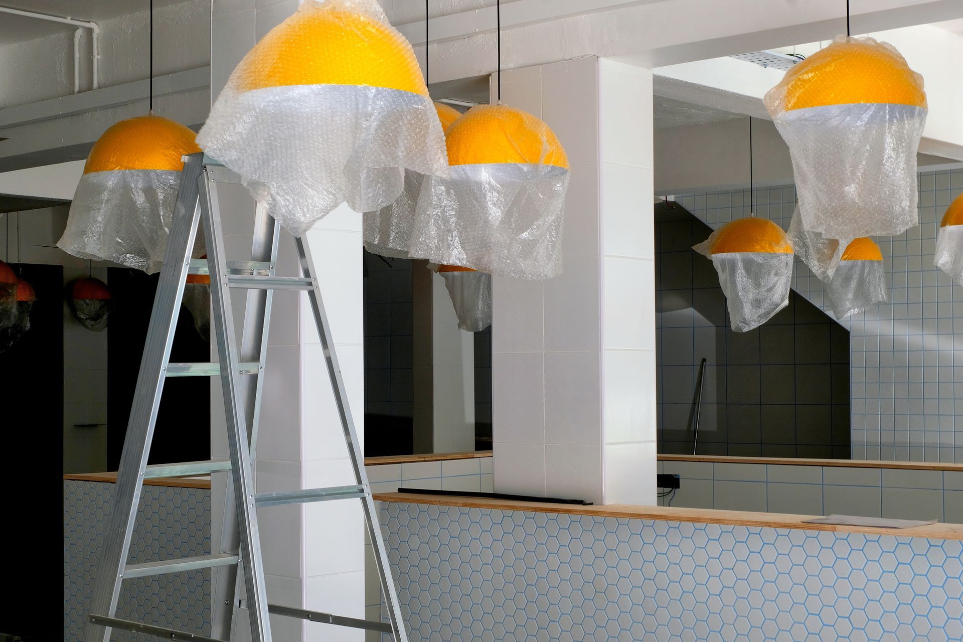 Orange dome pendant lights hanging in a mirrored room, with a ladder in the foreground