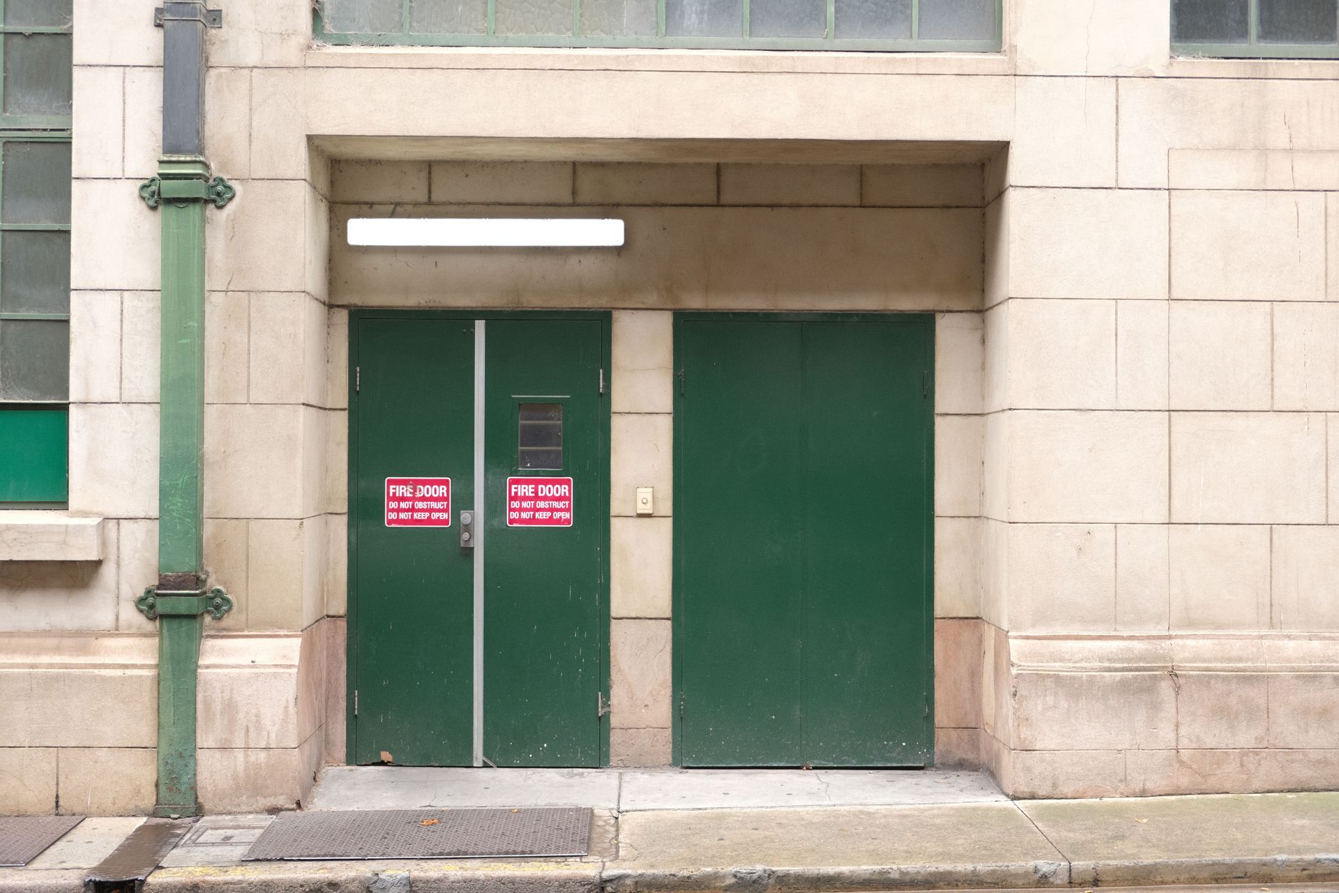 Green double doors in a stone building facade with red warning signs above a sidewalk.