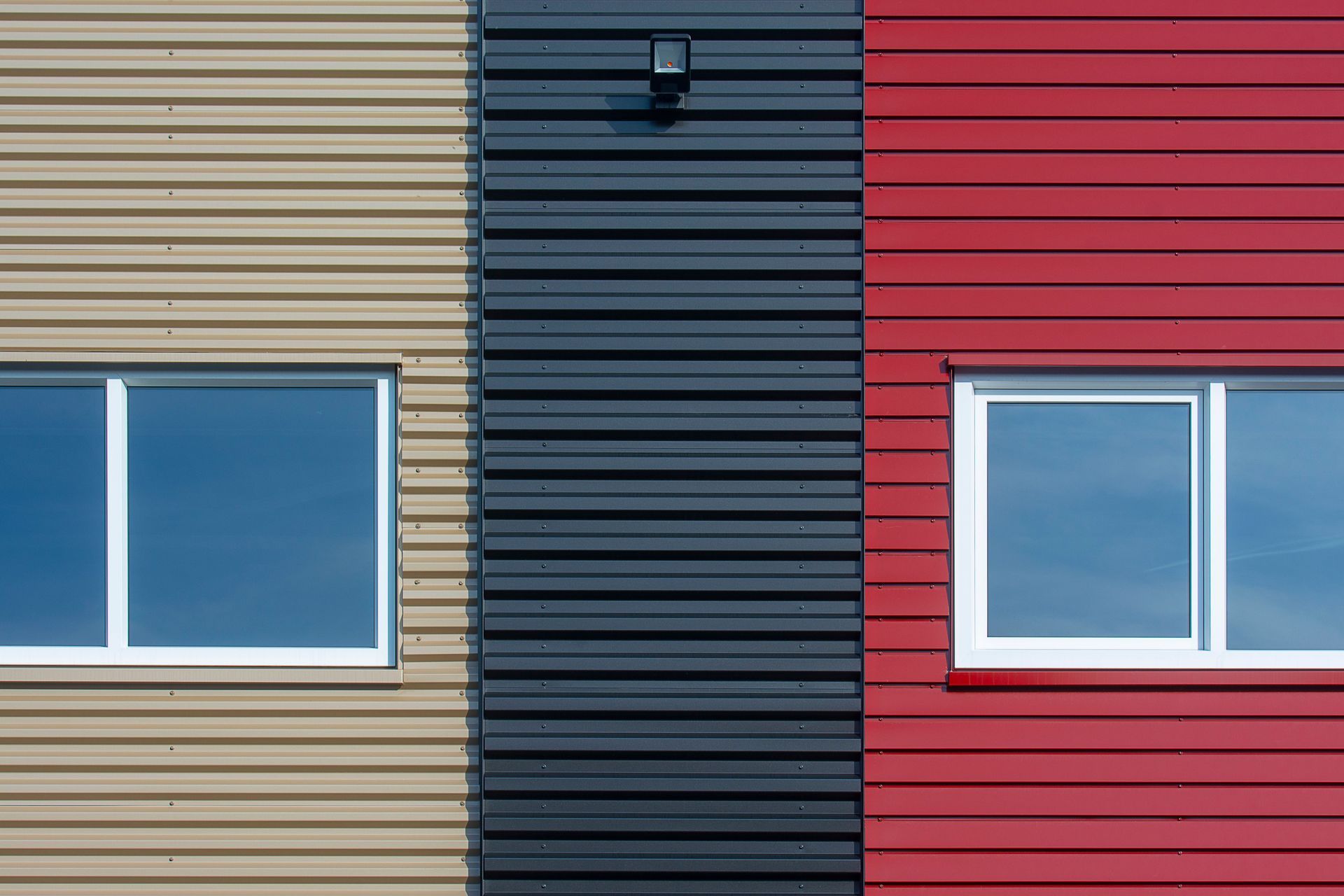 Colorful building facade with beige, black, and red panels and two windows