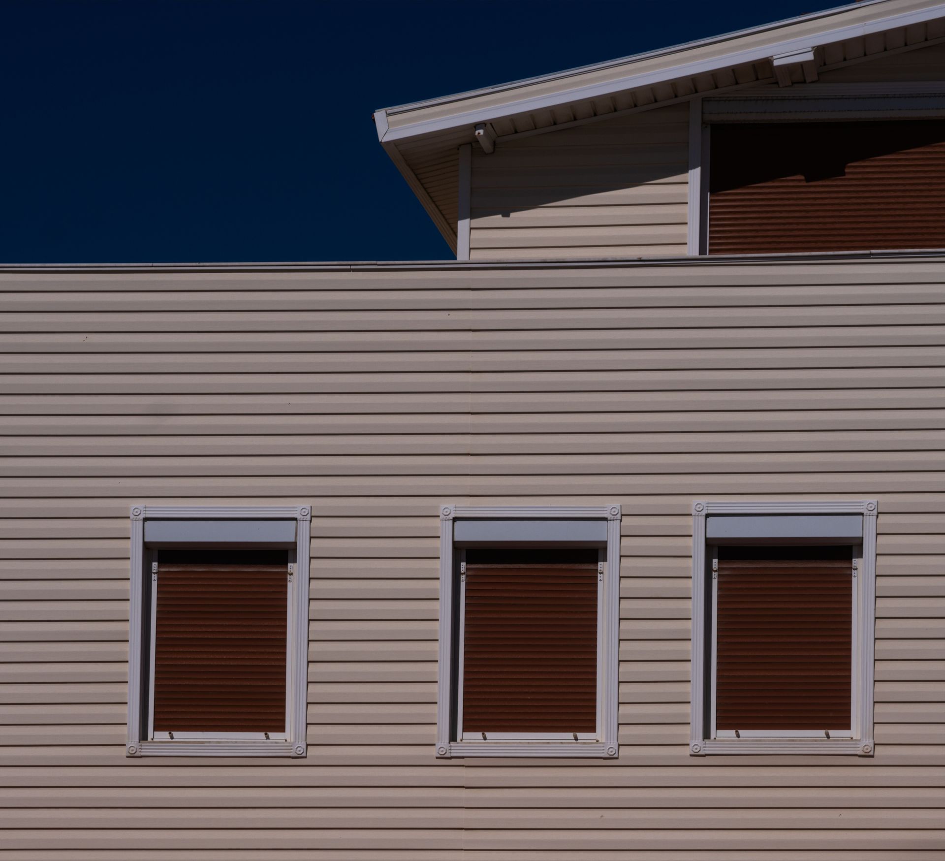 Beige house facade with three small windows under a dark blue sky