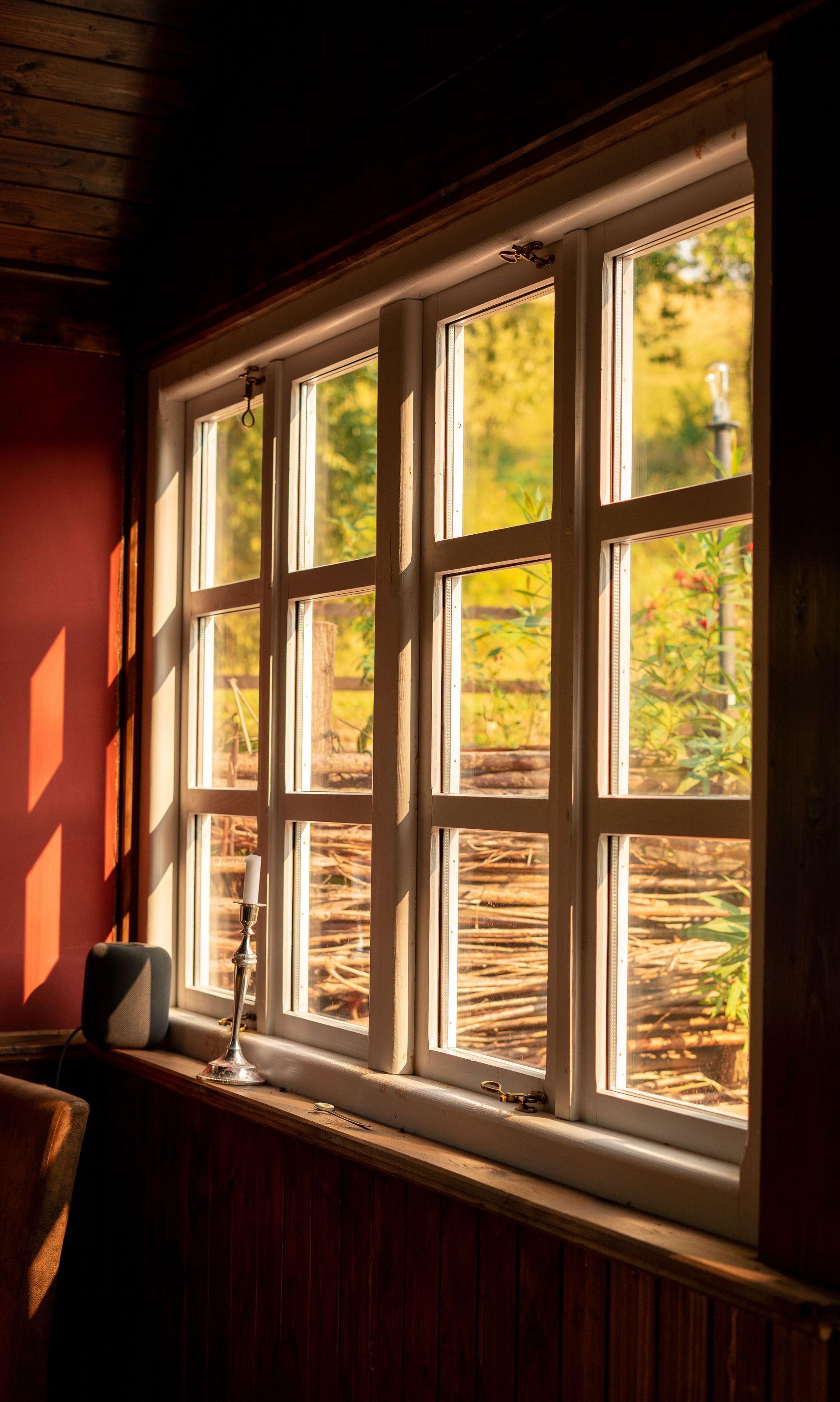 Sunlit wooden window with white panes, casting warm light onto a room with autumn leaves outside