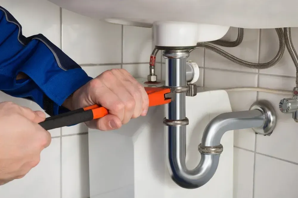 Person using a pipe wrench to fix a bathroom sink drain under a white basin
