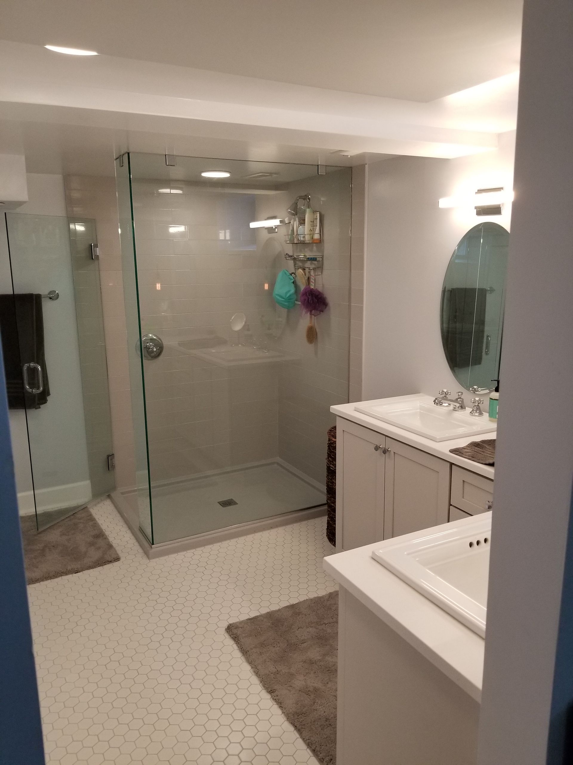 Modern bathroom with glass shower, white sinks, and gray accent rug.