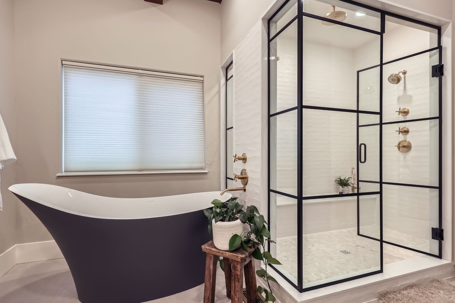 Bathroom with black framed shower and tub. White walls, gold fixtures, and potted plant.