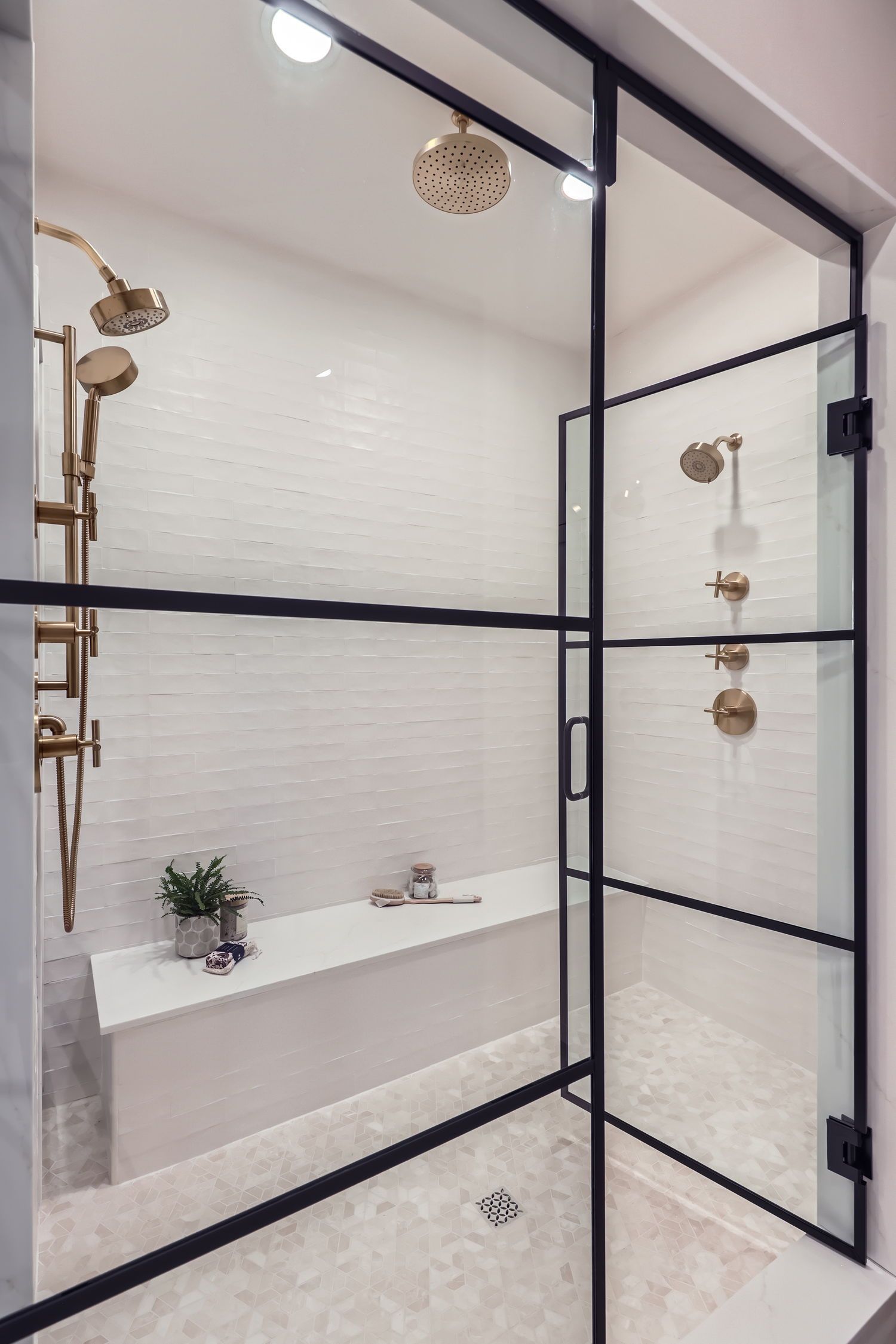 Modern bathroom with glass shower enclosure, white tile, gold fixtures, and a built-in bench.