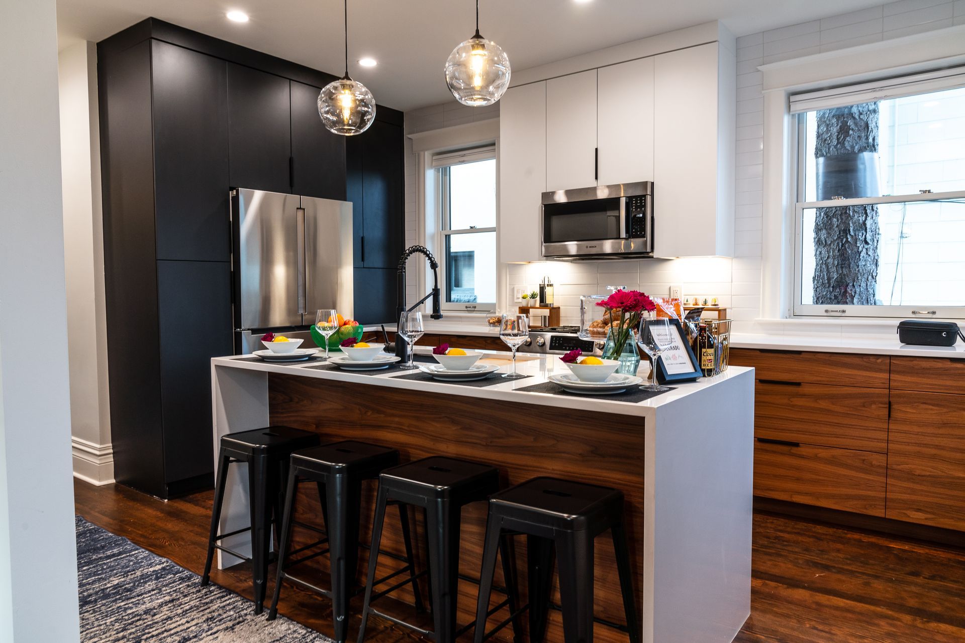 Modern kitchen with black and white cabinets, island with stools, stainless steel appliances, and wood floors.