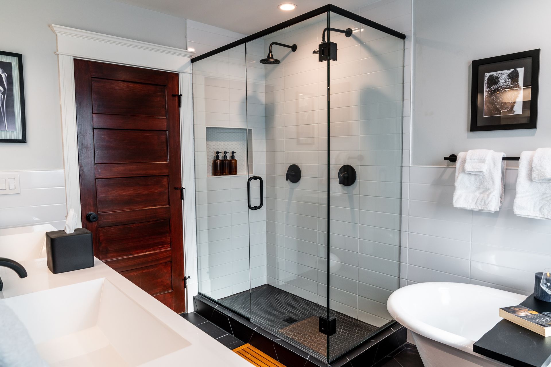 Modern bathroom with glass shower, white tile, dark wood door, and a white bathtub.