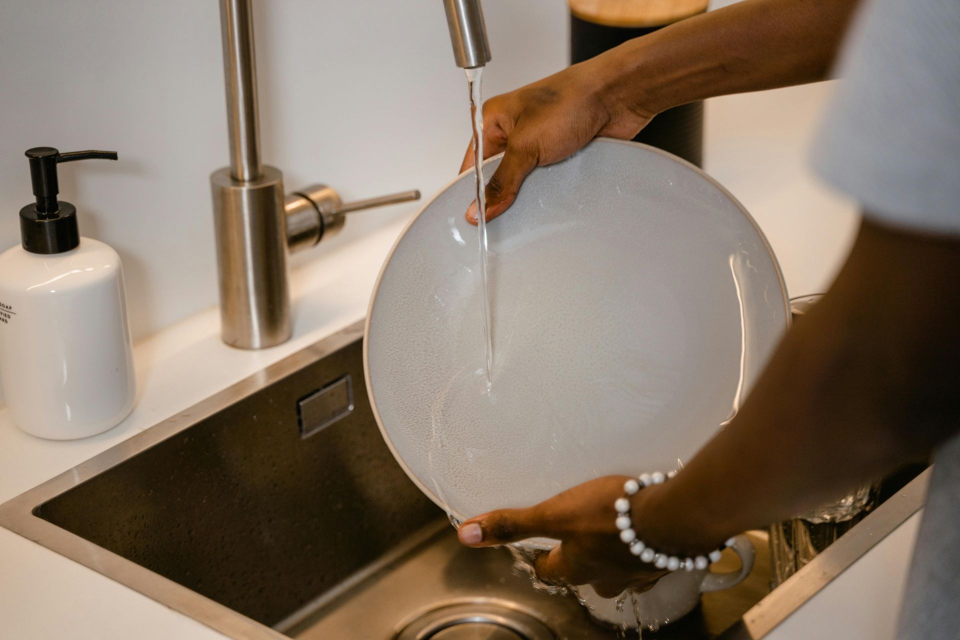 Person washing a white plate in a stainless steel sink, water running.