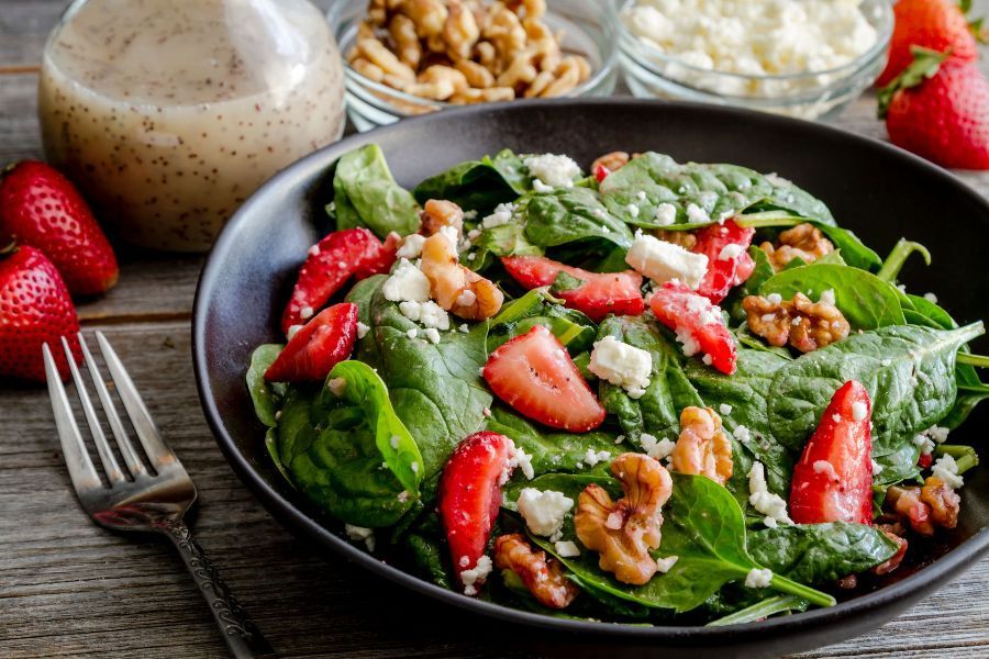 a salad with spinach , strawberries , walnuts and cheese in a black bowl with a fork .