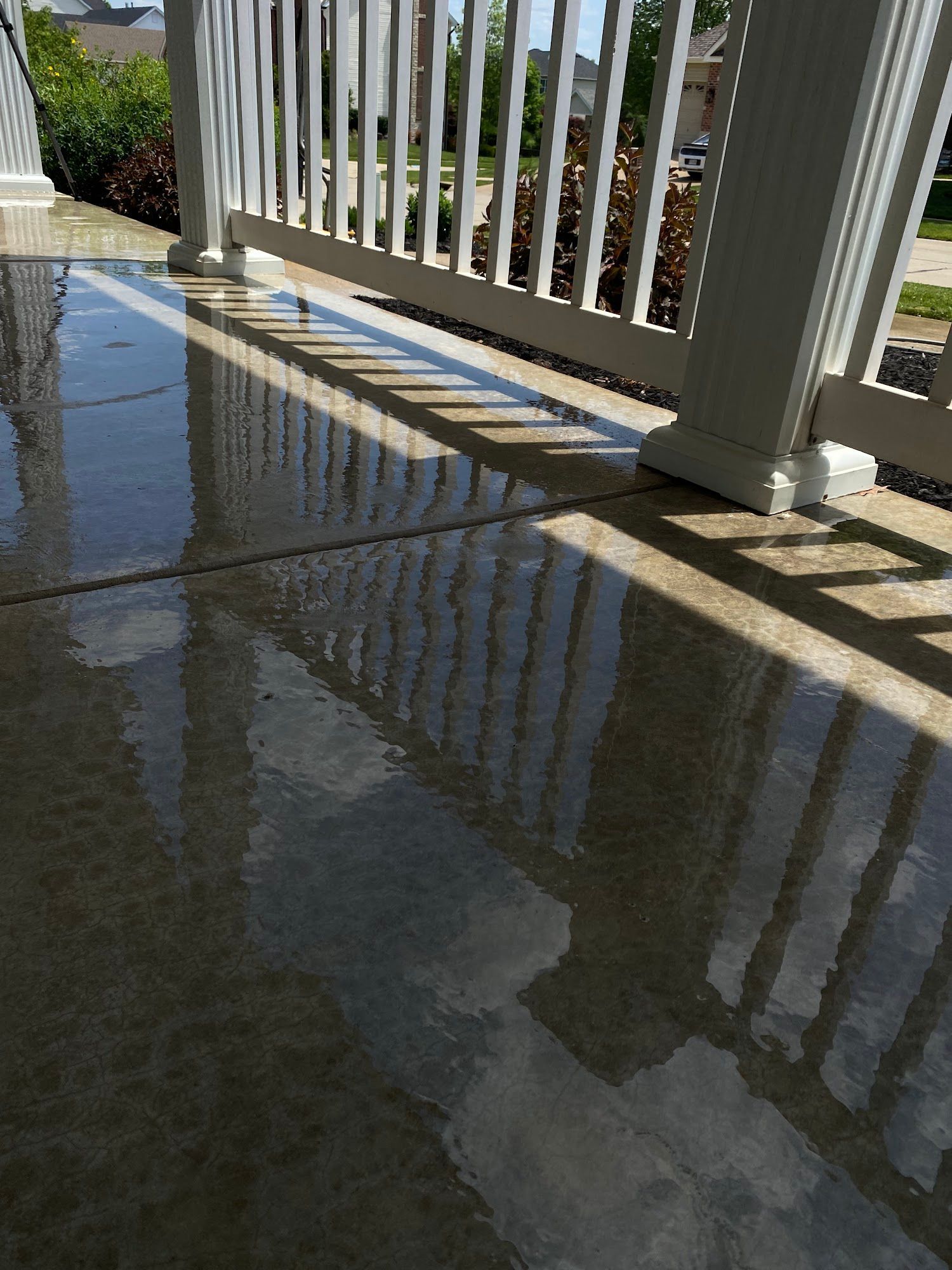 Wet, reflective concrete porch with white railing, casting shadows in bright sunlight.